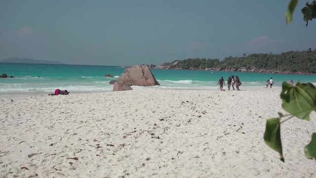 Seychelles. Praslin Island. Group of African American girls having a rest on the beach of an exotic island in the Indian Ocean. One woman shoots on camera as her friends bounce up.
