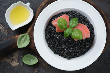 Top view of squid-ink risotto with salmon fillet, green basil and olive oil, studio shot