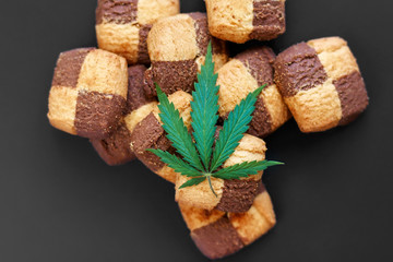 Hemp biscuits on a dark background with a green leaf of cannabis. Marijuana CBD dessert. Copy space. View from above