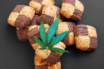 Breakfast with sweet cookies on a dark background with a green leaf of cannabis. Marijuana CBD dessert. Copy space. View from above. Concept of marijuana use for medicinal purposes