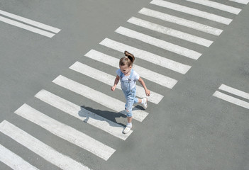 In the summer on the street at the pedestrian crossing kid girl in fashion clothes cross the road. From top view. Shadow at zebra crossing © Igor