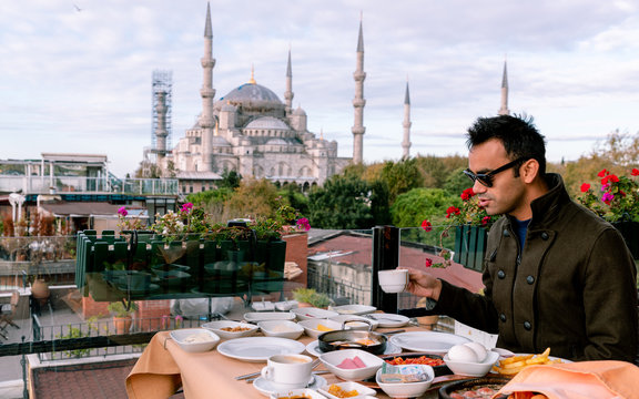 man in brown jacket sitting by the table holding white ceramic cup