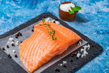 Fresh salmon with spices  in a black plate over light blue slate.