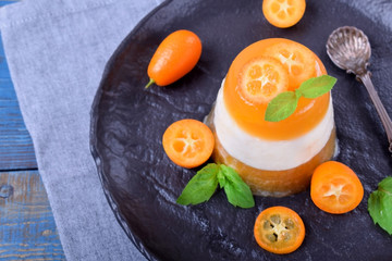 Layered dessert with fruits and yogurt on the black plate surrounded by kumquats and mint
