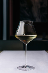 A beautiful glass on a long thin leg with white wine on a purple tablecloth.