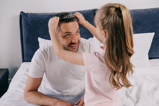 cute daughter putting diadem on happy dad on fathers day