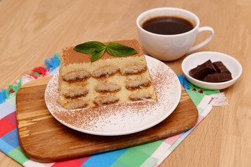 Tiramisu cake with coffee and fresh mint, on a plate on a light wooden background. Selective focus.
