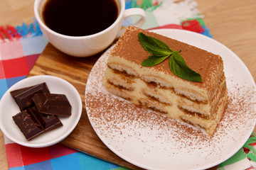 Tiramisu cake with coffee and fresh mint, on a plate on a light wooden background. Selective focus.