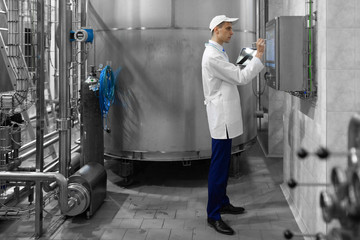 Portrait of man in a white robe and a cap standing in production department of dairy factory with laptop
