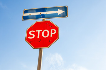 Old scratched road signs - stop and direction of movement against the blue sky and copy-space. Stop...