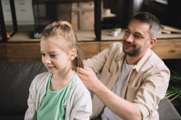 selective focus of happy father weaving daughters hair at home