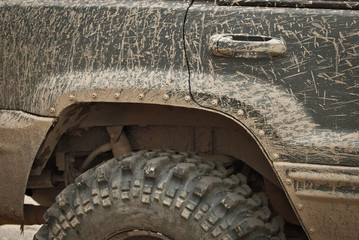 Wheels, lights and bumper are laced in a swamp. Dirty parts of a truck close up.