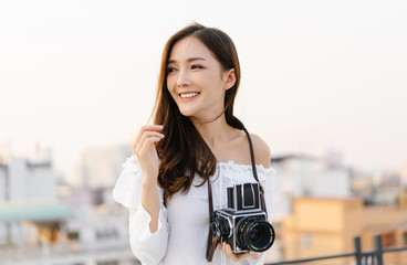Portrait of young Asian smiling woman model with retro film camera  and looking away on the rooftop...