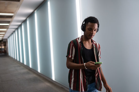 attractive young handsome guy walks in the neon light of the night city listens to music in wireless headphones from a mobile phone and dances fun