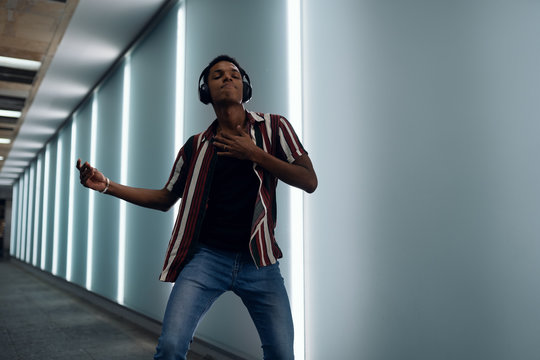 attractive young handsome guy walks in the neon light of the night city listens to music in wireless headphones from a mobile phone and dances fun