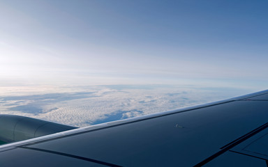 Fototapeta na wymiar Aviation: View over the wing of a modern airplane above the clouds over the sea on a sunny winter day