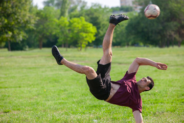 Young man playing football in park keeping ball in the air