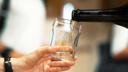 Close up and selective focus view hand holding a glass and bottle pouring white wine to taste, winery tasting.