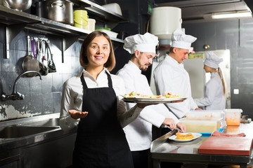 Fototapeta na wymiar happy woman waiter collecting dishes from restaurant’s kitchen