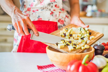 Female hand put cut eggplant in wooden bowl in kitchen. Cooking vegetables