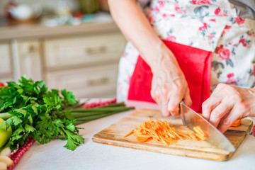 Female hand with knife chops carrot in kitchen. Cooking vegetables