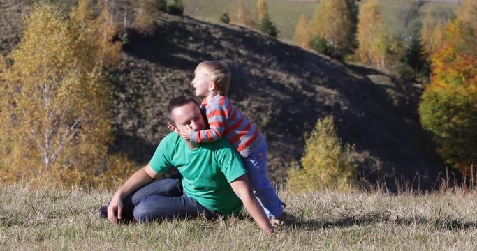 Little child kiss and hug father in autumn nature, colorful foliage