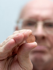 An old man holds in his hand a coin of two euro cent.