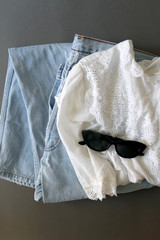 Fashionable outfit with vintage white blouse and washed out jeans. Flat lay, gray background.
