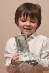 Happy child with money dollar, little businessman. Pile of United States dollar hundred USD banknotes in boy's hand.