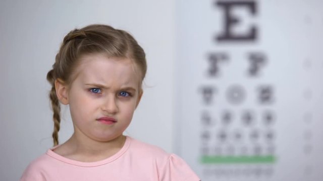 Little girl trying to read letters from eye chart, diagnostic of nearsightedness