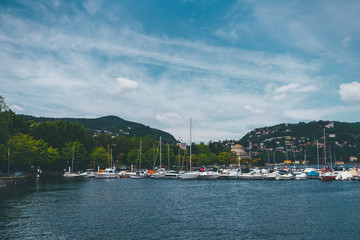 Fototapeta na wymiar View of yachts in the lake against the background of mountains covered with greenery and blue sky,