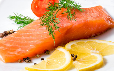 Pieces of red fish with lemon and cherry tomatoes on a white background