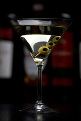 Vodka martini cocktail with olives in bar on black