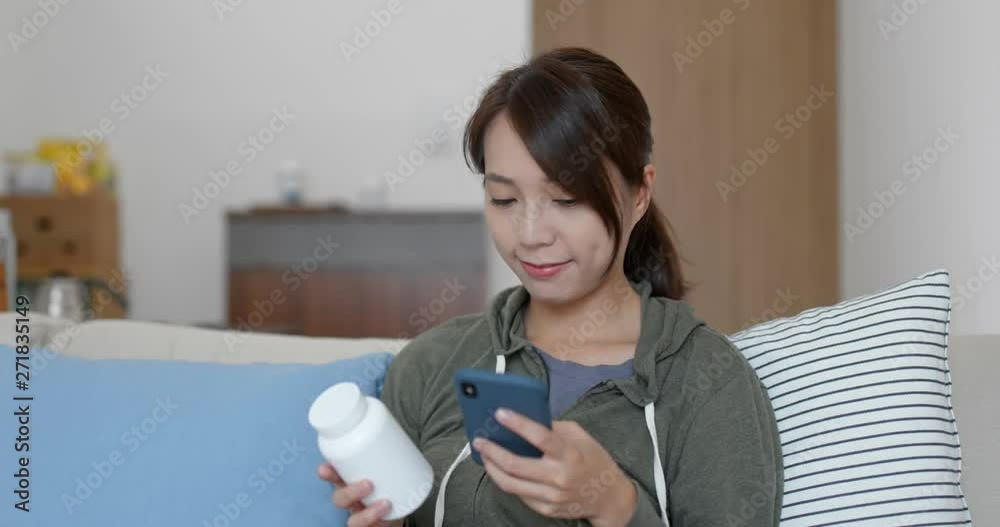 Wall mural Woman checking the bottle of medicine on cellphone at home