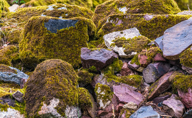 various brown and mottled boulders close up, stacked, some of them overgrown with moss and grass
