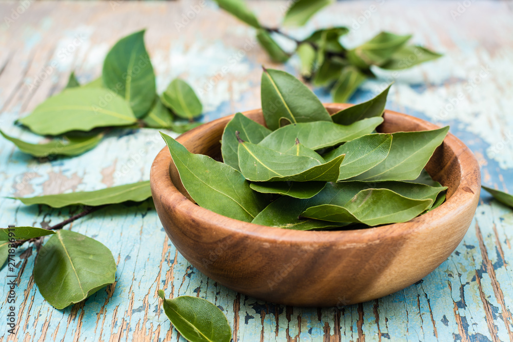 Wall mural Fresh leaves of bay leaves in a bowl and next to it on a wooden rustic table