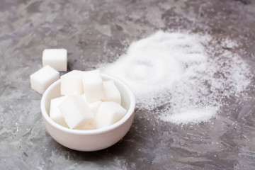 Pieces of refined sugar in a bowl and next, a pile of sugar sand on the table