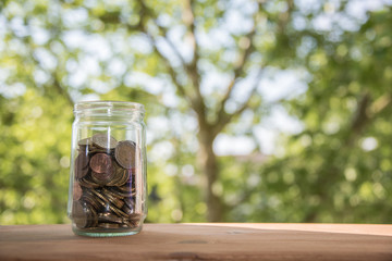 A glass full of coins. Save money to grow your finances. Many small amounts are a good plan to make a profit. Natural background and wooden table.