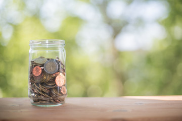 A glass full of coins. Save money to grow your finances. Many small amounts are a good plan to make a profit. Natural background and wooden table.