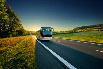 Foto op Plexiglas White bus traveling on the asphalt road around line of trees in rural landscape at sunset © am