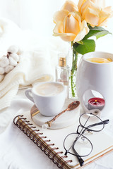 Morning coffee mug with glasses on a notebook, candle and rose on a white bed top view . Woman cozy morning