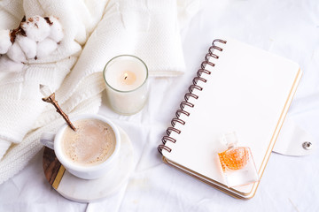 Morning coffee mug with notebook, candle and cotton flowers on a white bed top view . Woman cozy morning