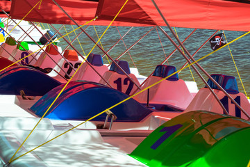 Multi-colored catamarans on the river bank. Catamaran with numbers and red roof. Water transport...