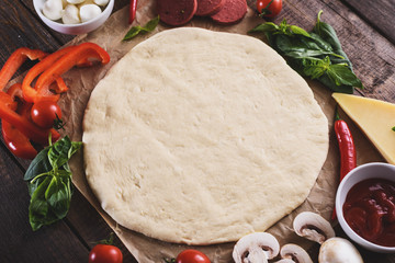 Top view of raw rolled pizza dough with ingredients on wooden table