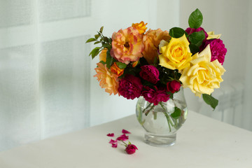 Beautiful Bouquet of summer orange yellow and purple English roses in glass vase, jar near the big white window on table.