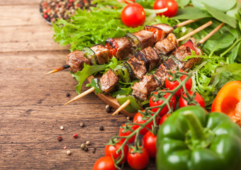 Grilled pork and chicken kebab with paprika in round wooden plate of lettuce salad, on wooden background with tomatoes and paprika pepper and spinach.