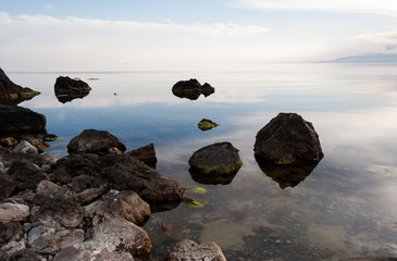 Boulders and rocks in the water. Beautiful seashore with different stones. Blue sky with clouds reflection in water. Nature composition. 