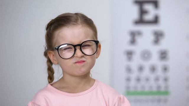 Capricious little girl rejecting eyeglasses from optician, feels insecure, shy