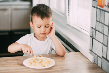 a child in the kitchen during the day eating pasta in a spiral in a white t-shirt