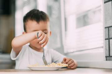 a child in the kitchen during the day eating pasta in a spiral in a white t-shirt